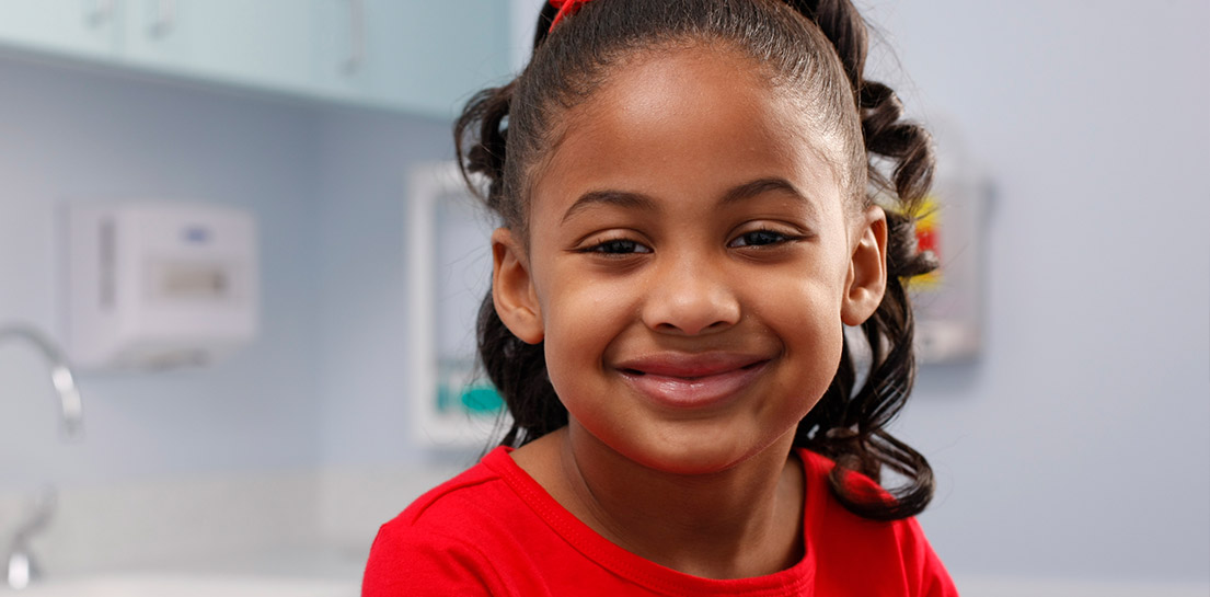 Happy young girl in a red shirt smiles at the viewer in a clinic