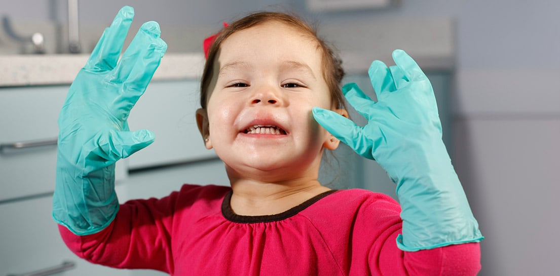 Smiling toddler wearing oversized blue medical gloves, hands raised