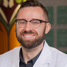 Smiling man with glasses and beard, wearing a white lab coat